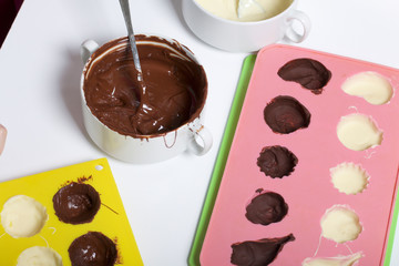 Melted white and black chocolate in white cups. Nearby silicone mold smeared with chocolate.