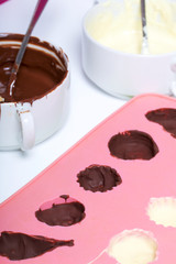 Melted white and black chocolate in white cups. Nearby silicone mold smeared with chocolate.
