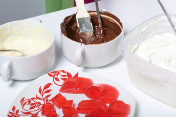 Melted white and black chocolate in white cups. Blender-ground curd and strawberry jelly on a plate. Stand for making dessert.