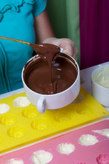 A woman using a brush brushes a silicone dessert mold with a melted black chocolate.