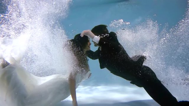Passionate couple lovers dive simultaneously under water with splashes and bubbles. woman in wedding dress