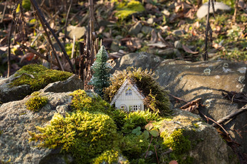 Christmas and New Year miniature house at forest in the sunlight. Little toy house close up. Festive background. Christmas decorations. Holiday and celebration concept.