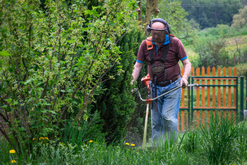 Senior man mowing grass by brushcutter in garden at springtime