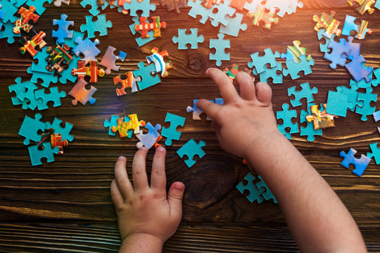 child's hands collect cardboard puzzles on a wooden background. logic, pre-school education.