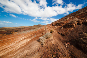 Amazing vulcanic landscape with mountains. Sky is blue with clouds, gravel is red and brown. Fuerteventura Island, Canary Island, Spain, Europe.