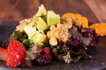 Green salad with strawberry, blackberry, blood oranges, alligator pear, beets, seeds and nuts on a wooden background, selective focus, free space. Delicious healthy food.