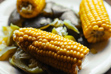 Macro close-up of boiled corn and vegetables on a white plate with focus on the cob