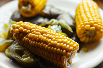Macro close-up of boiled corn and vegetables on a white plate with focus on the cob
