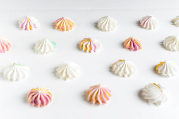 Pattern with meringues on a white wooden background. Multicolored meringues on a white background. Basis for confectionery banner, cafe, sweet shop. Meringue banner