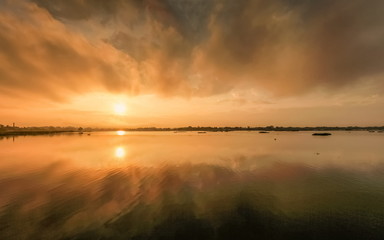 Lake view morning of dark cloud moving above the lake with reflection on the water and colorful of yellow sun light in the sky background, sunrise at Kwan Phayao Lake, Phayao, northern of Thailand.