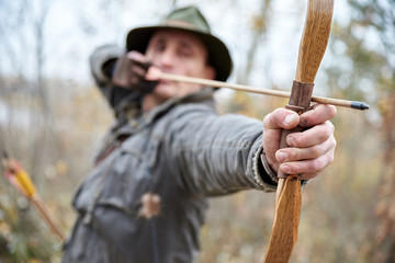 MAN IN THE HAT SHOOTS FROM WOODEN BOW ON OUTSIDE, IN AUTUMN