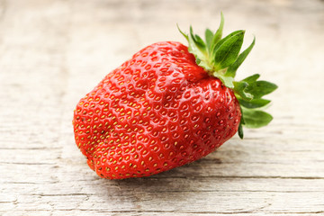 Large red and ripe strawberry on a wooden surface. Close-up.