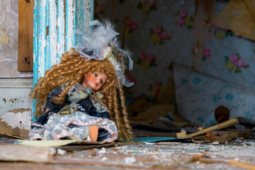 An old doll sittibg against the door frame in an abandoned house. Debris litters the floor, and...