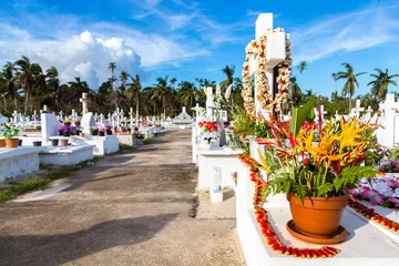 Fotobehang White crosses of a christian cemetery, Uvea (Wallis) island, Wallis and Futuna territory (Wallis-et-Futuna), French overseas collectivity. Strelitzia flowers bouquet on a tomb on the foreground © Dmitry