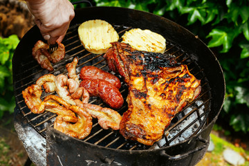 Hand man takes a sausage with a fork on a barbecue grill meat