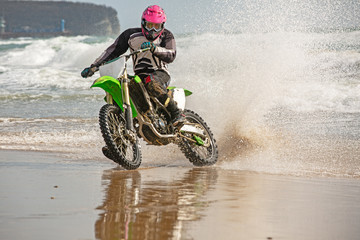 Obraz premium Motorcyclist in a protective suit rides a motorcycle on the sea, splashes fly from under the wheels.