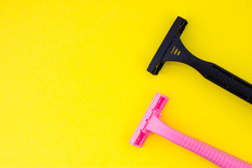 Two disposable razors in black and pink color are on yellow uniform background view from above with clear area of half of photo for labels or headers. Hygienic products for hair removal for women 
