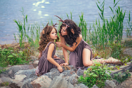 family photo of mother and child, fauns on the shore of a large lake are sitting on stones, fairy-tale characters, the mother reaches out for her daughter, while the baby looks around with interest