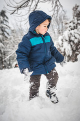 Fototapeta na wymiar Adorable, cute, little boy walking in the snow in blue jacket