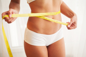 Hands measuring waist with a tape. Slim and healthy woman at her home
