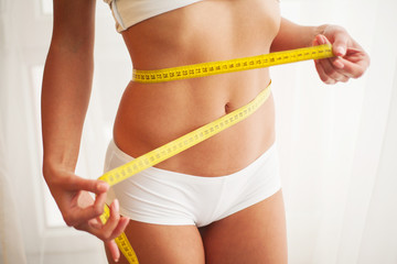 Hands measuring waist with a tape. Slim and healthy woman at her home