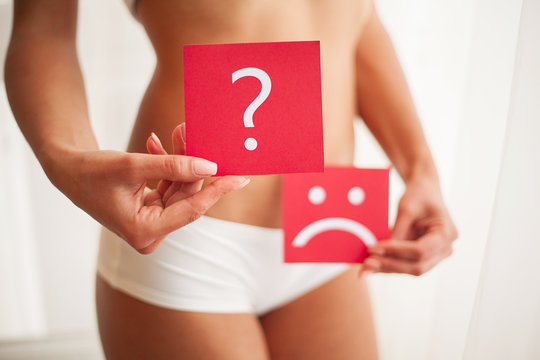 Woman Health Problem. Closeup Of Female With Fit Slim Body Holding Cards With Sad Smiley Face And Question Mark Near Her Stomach. Digestive Disorders, Period Pain, Health Issues Concept