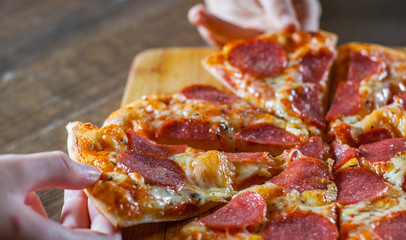 two woman Hand takes a slice of Pepperoni Pizza with Mozzarella cheese, salami, Tomatoes, pepper. Italian pizza on wooden table background