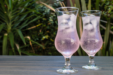two glasses of pink craft gin and tonic on a wooden table in a garden setting