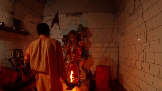 Aarti Hindu religious ritual of worship monk in orange clothes with light in hand in front of statue of Hanuman monkey God automatic machine works evening