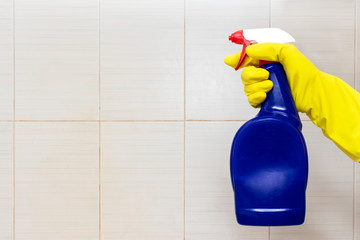 Hand in yellow rubber glove holding a blue cleaning spray bottle close up with copy space. Washing, cleaning and wiping concept