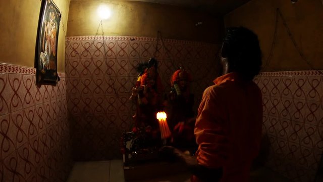 Hindu monk performs evening aarti to Krishna's and Rukmini's statues rings bell and repeats movements with burning light fixture