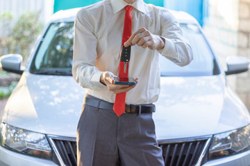 Businessmen offers a smartphone with a car key on automobile background. Car sharing mobile app...