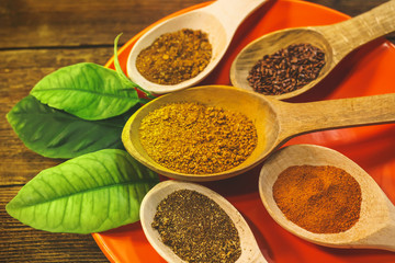 various spices in wooden spoons on an orange plate with lemongrass leaves. kari, chilli peppers, dry spices, flax seeds, pumpkin seeds. wooden table.