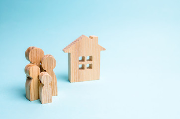 family stands near a wooden house on a blue background. The concept of affordable housing and...