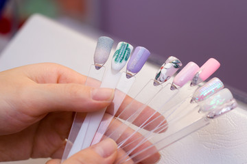 Manicure and nail care concept. A woman in a beauty salon holds colored test nail polishes with different colors and chooses the color for painting