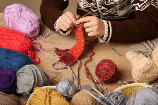 Child boy is learning to knit. Colorful wool yarns are on the wooden table. Hand closeup.