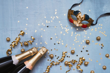 Two champagne bottles with carnival mask, confetti stars and party streamers on blue background....