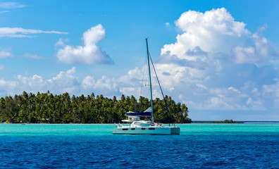 Lonely catamaran in the turquoise lagoon on the background of the island of Tahaa in the Leeward...