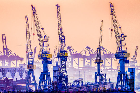 Cranes In Hamburg Harbor, Germany, Seen Against The Late Evening Sky.