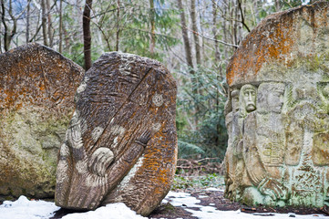 Ancient large stones with engraving at green forest with little snow cover in Carpathians mountains.