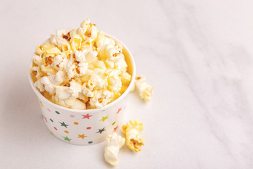 Tasty salty popcorn in paper cup on light marble backgraund