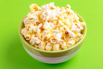 Tasty salty popcorn in bowl on bright green backgraund