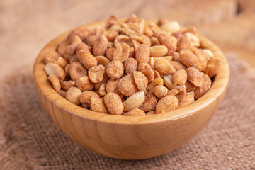 Roasted peanuts in wooden bowl on burlap napkin