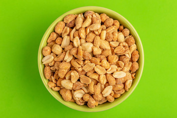 Roasted peanuts in bowl on bright green background