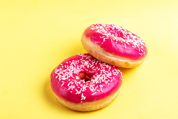 Two delicious pink donuts with sprinkle on bright yellow background