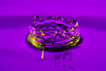 High speed capture of a droplet with crown hitting the water surface in purple and yellow.