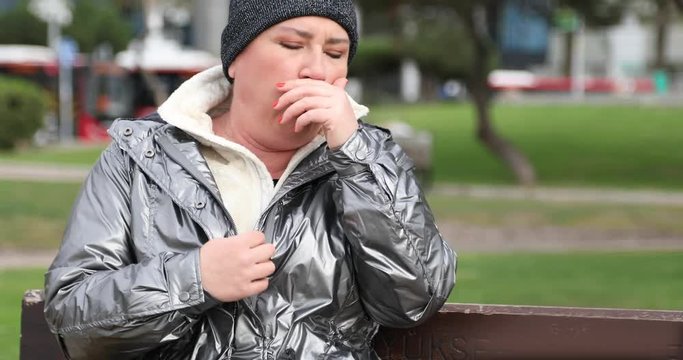 Sick woman sneezing during cold day wearing warm clothes outdoor