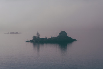 Lonely house on small island in mist. Foggy landscape.