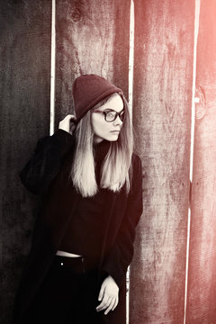 Stylish hipster model in glasses and hat holding hair. Toned picture of lonely teenager on a cold autumn day