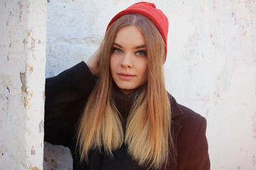 Young beautiful girl with a blond hair in red hat leaned to white wall